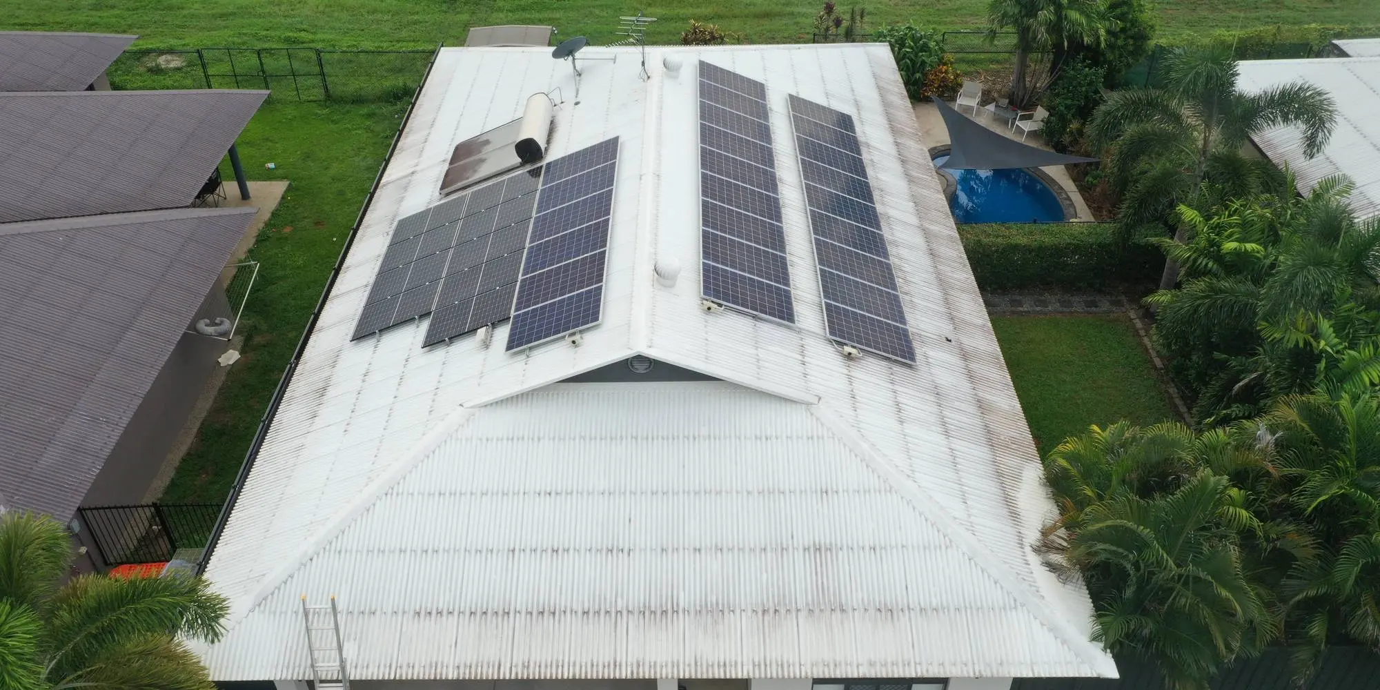 An aerial view of a Darwin house with a cleaned metal roof and solar array, surrounded by tropical garden and a pool
