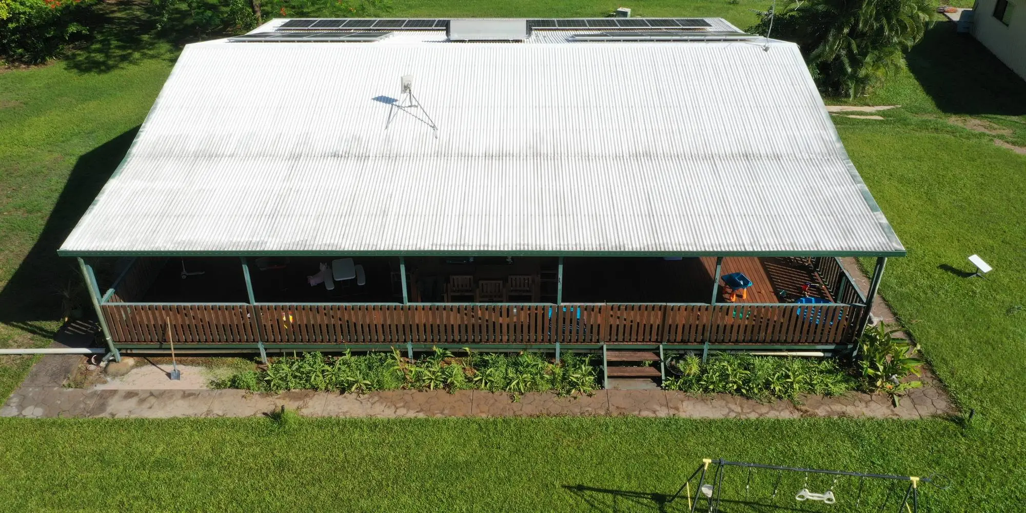 An aerial view of a long verandah house with a freshly soft washed metal roof on green lawn