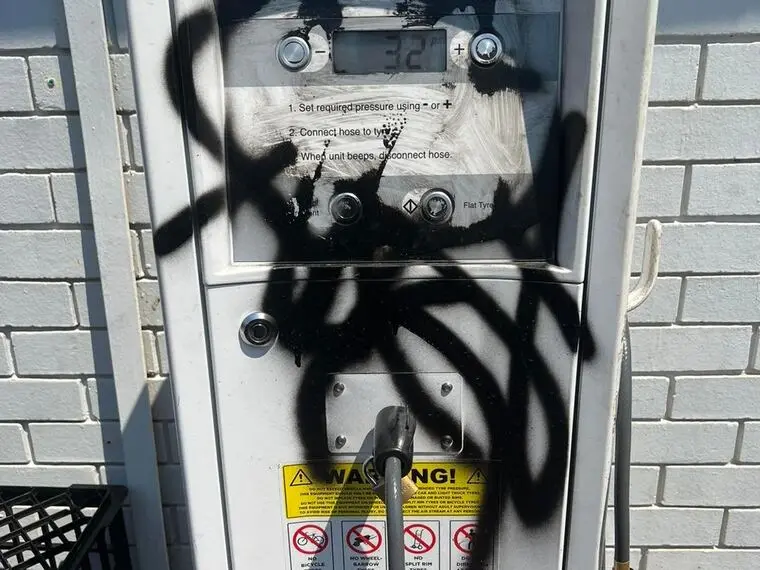 Black spray paint tagged across a painted block wall before graffiti removal