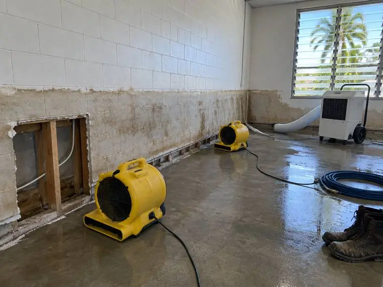 A flood damaged room being dried out, with a tide line up the blockwork, an air mover on the wet slab and a dehumidifier ducted to the wall