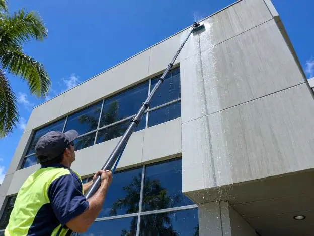 An operator washing the upper cladding of a three storey building from the ground with a telescopic water fed pole