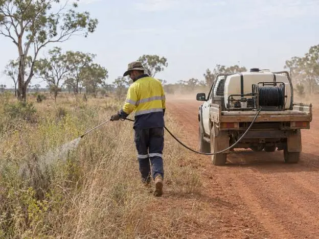 An operator treating weeds along a red dirt road verge from a spray unit on the back of a ute