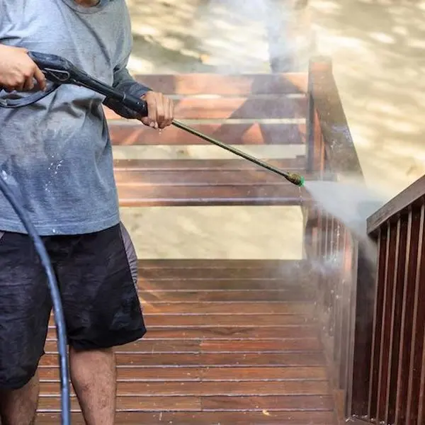 An operator pressure washing a timber deck, clean boards appearing behind the wand