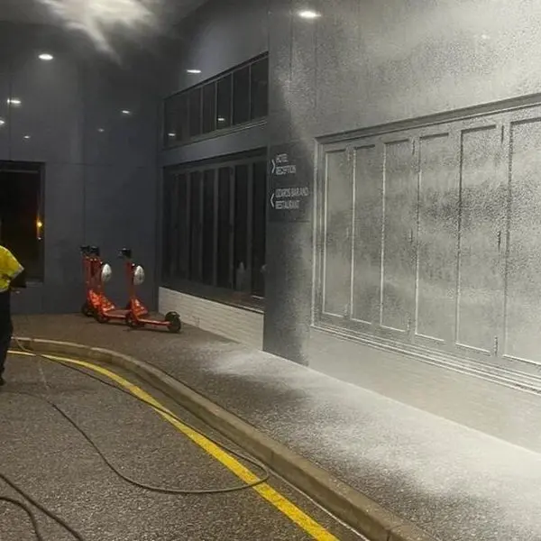 An operator rinsing down a warehouse wall, mist hanging in the air