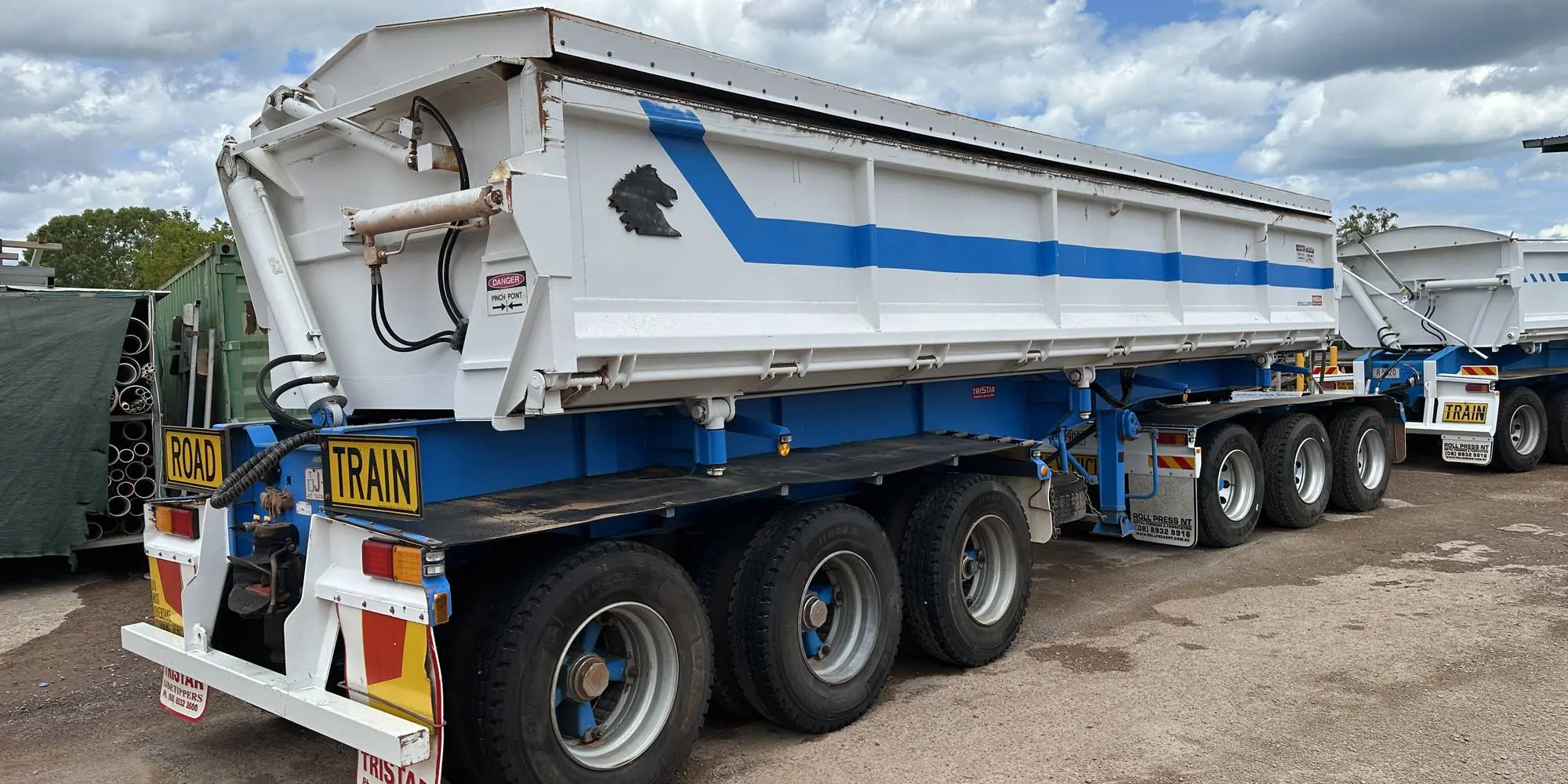 Two washed road train tipper trailers parked on red dirt at the Power Clean NT yard under a Territory sky
